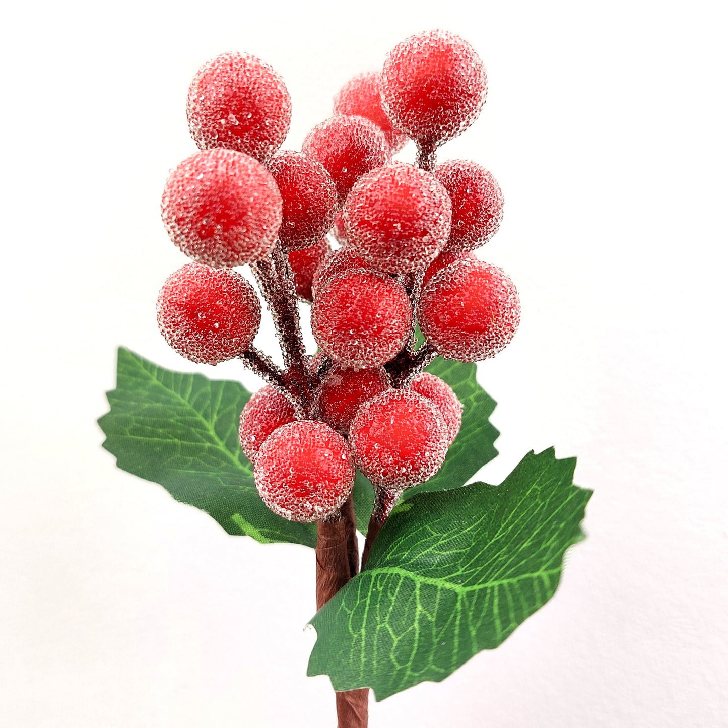 Artificial red berry branch with green leaves on a white background