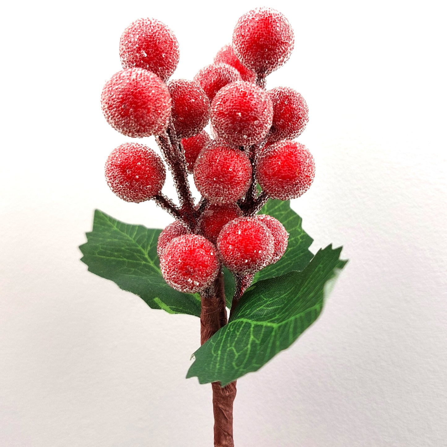 Artificial berry branch with red berries and green leaves on a white background