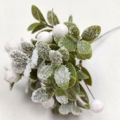 Close up of Faux Frosted green leaves and white berries on a white background