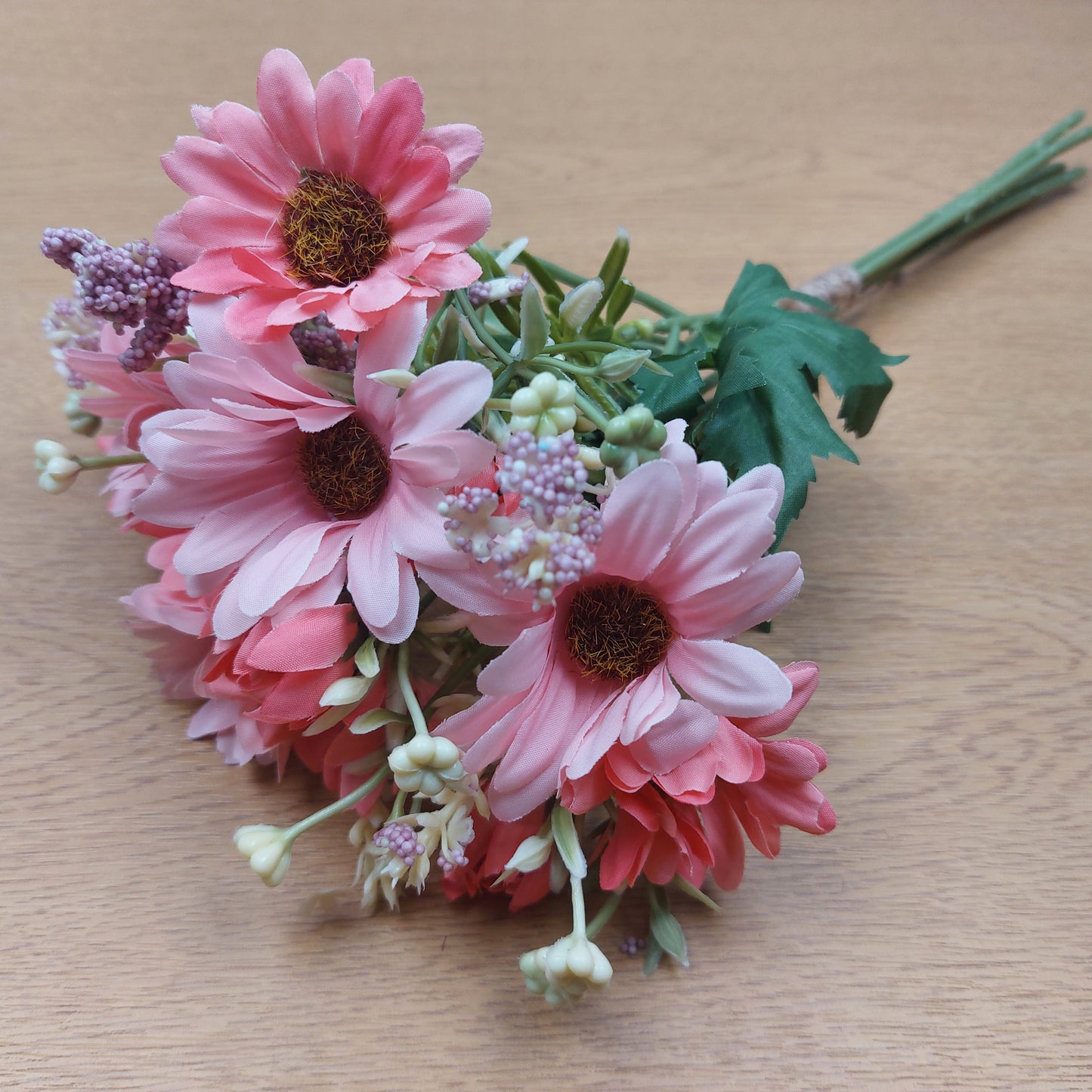 A bunch of artificial assorted Pink Gerbera Daisies and other greenery on a wooden background 