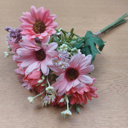 A bunch of artificial assorted Pink Gerbera Daisies and other greenery on a wooden background 