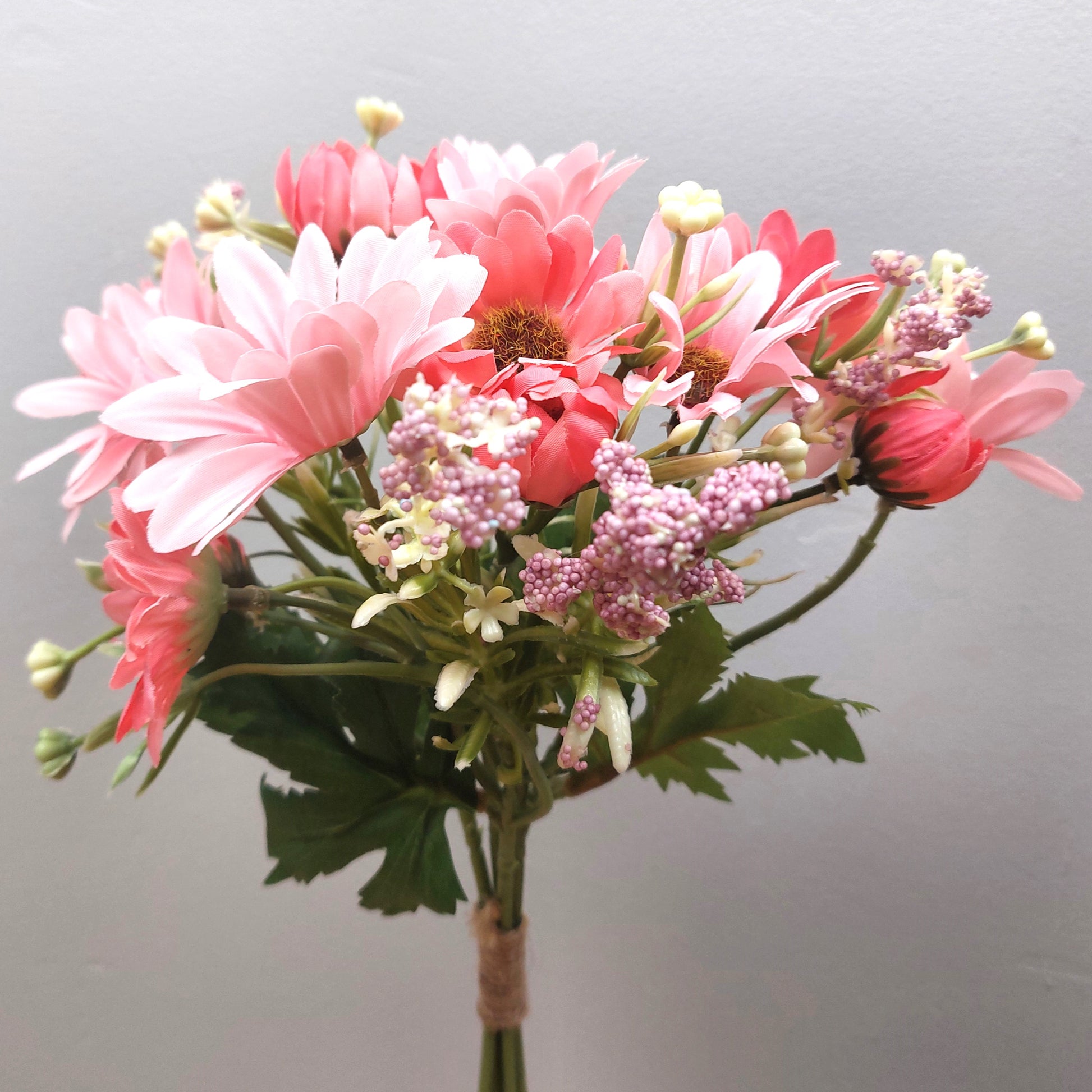 A bunch of artificial assorted Pink Gerbera Daisies and other greenery against a pale background