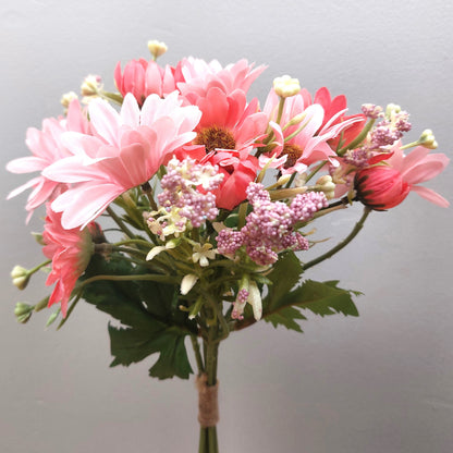 A bunch of artificial assorted Pink Gerbera Daisies and other greenery against a pale background