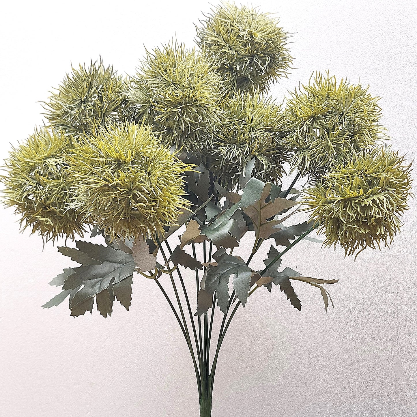 An artificial Green Trick Dianthus Pom Pom bush with foliage against a pale background