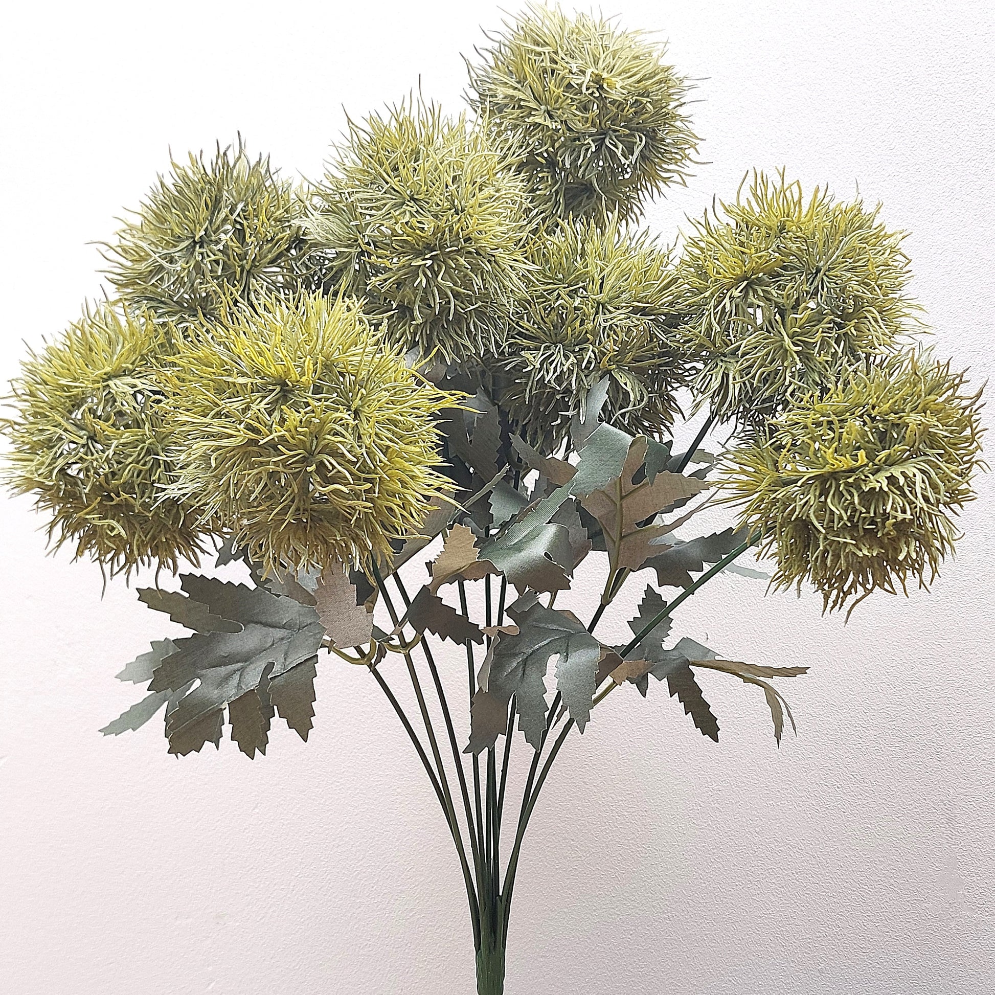 An artificial Green Trick Dianthus Pom Pom bush with foliage against a pale background