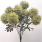 An artificial Green Trick Dianthus Pom Pom bush with foliage against a pale background