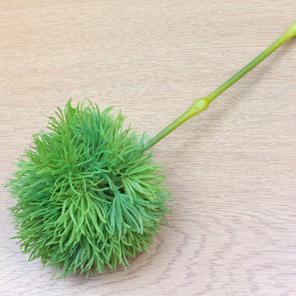Green decorative artificial Pom Pom ball with a stem on a wooden surface