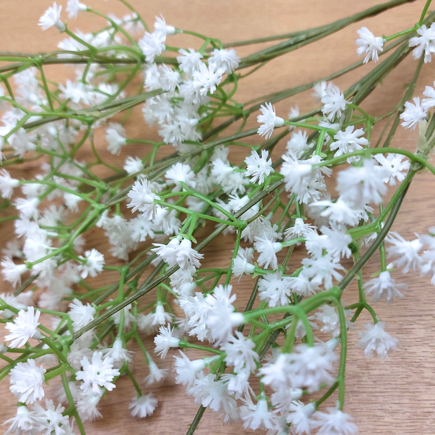 A close up of a Bouquet of artificial white flowers with green stems on a wooden surface