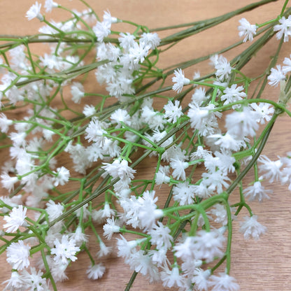 A close up of a Bouquet of artificial white flowers with green stems on a wooden surface