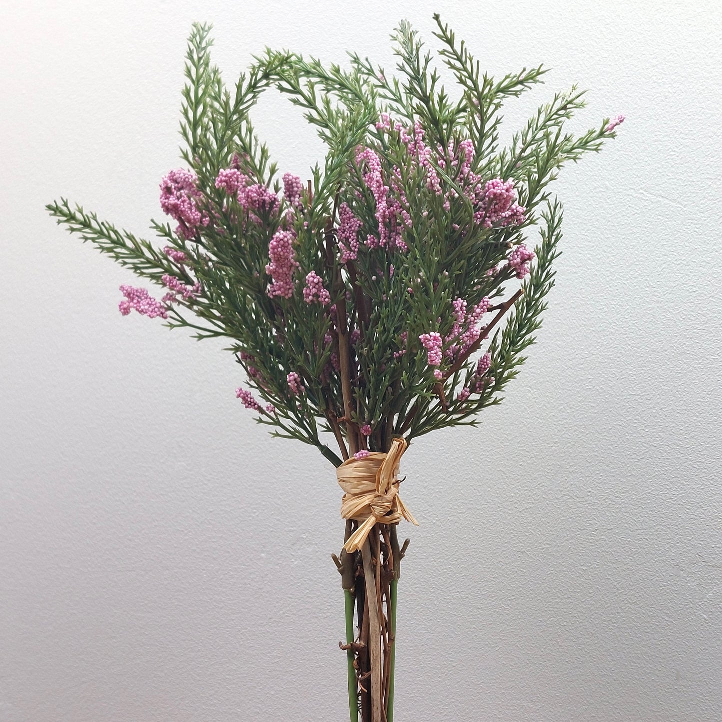 Bouquet of artificial pink heather flowers and green leaves tied with twine on a light gray background