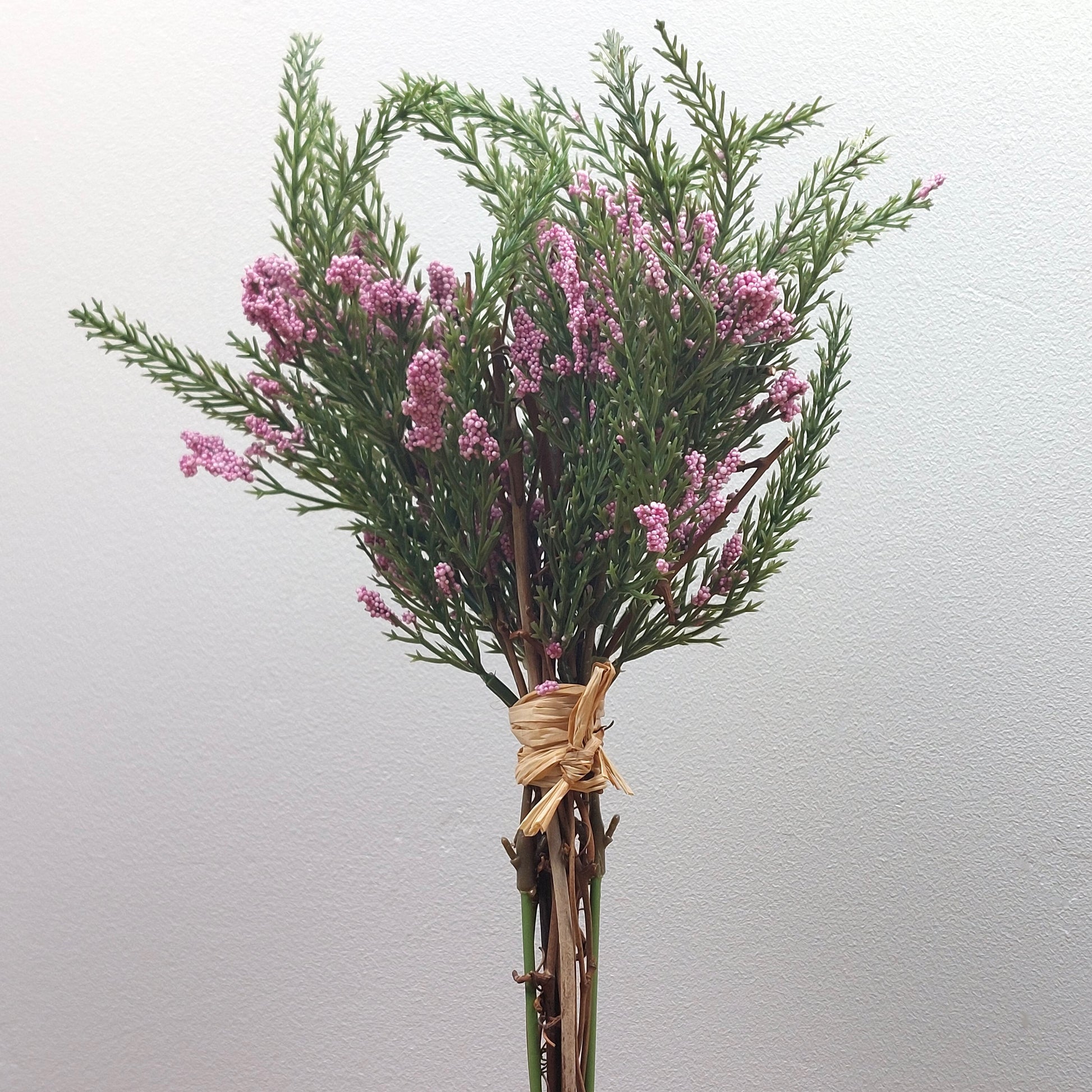 Bouquet of artificial pink heather flowers and green leaves tied with twine on a light gray background