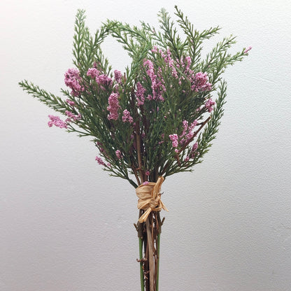 Bouquet of artificial pink heather flowers and green leaves tied with twine on a light gray background