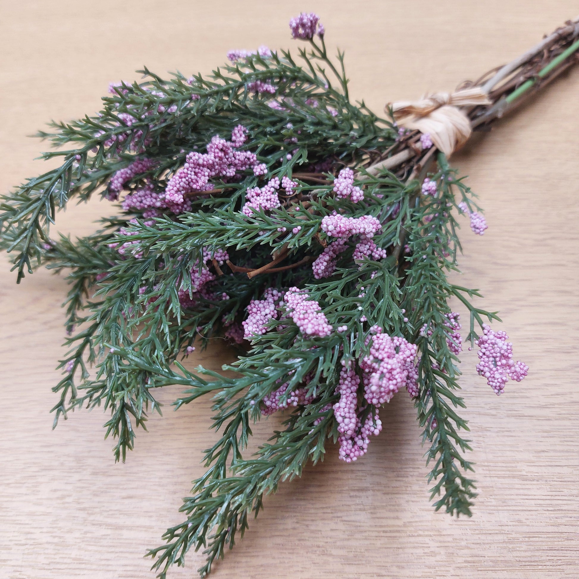 Bouquet of artificial greenery with purple heather flowers on a beige background