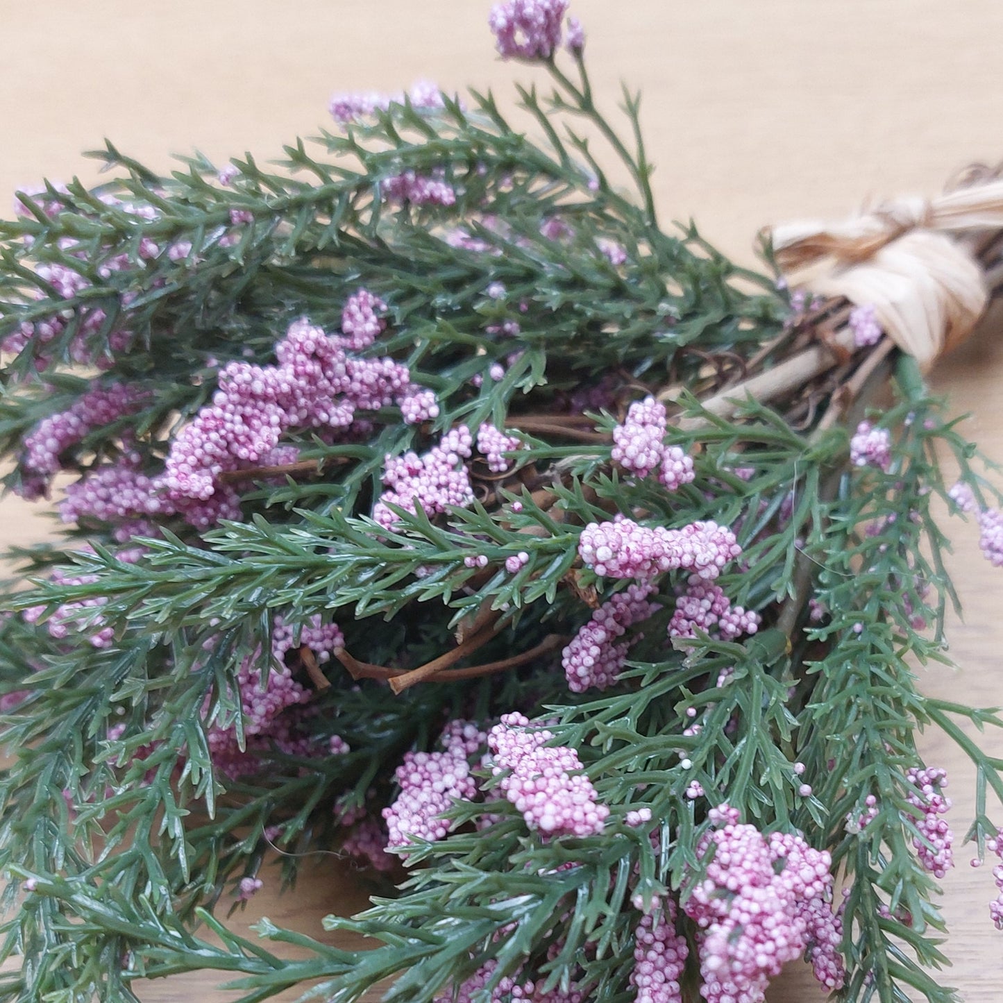 Close up of an artificial Bouquet of greenery with purple heather flowers on a wooden surface