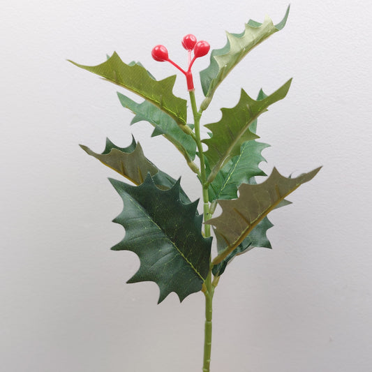 Artificial Holly branch with green leaves and red berries on a light gray background