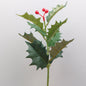 Artificial Holly branch with green leaves and red berries on a light gray background