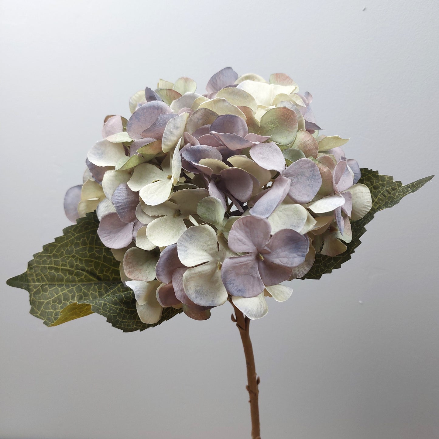 Artificial lilac hydrangea flower arrangement with green leaves on a light gray background