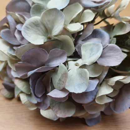 Close up of an artificial lilac Hydrangea flower head on a wooden surface.