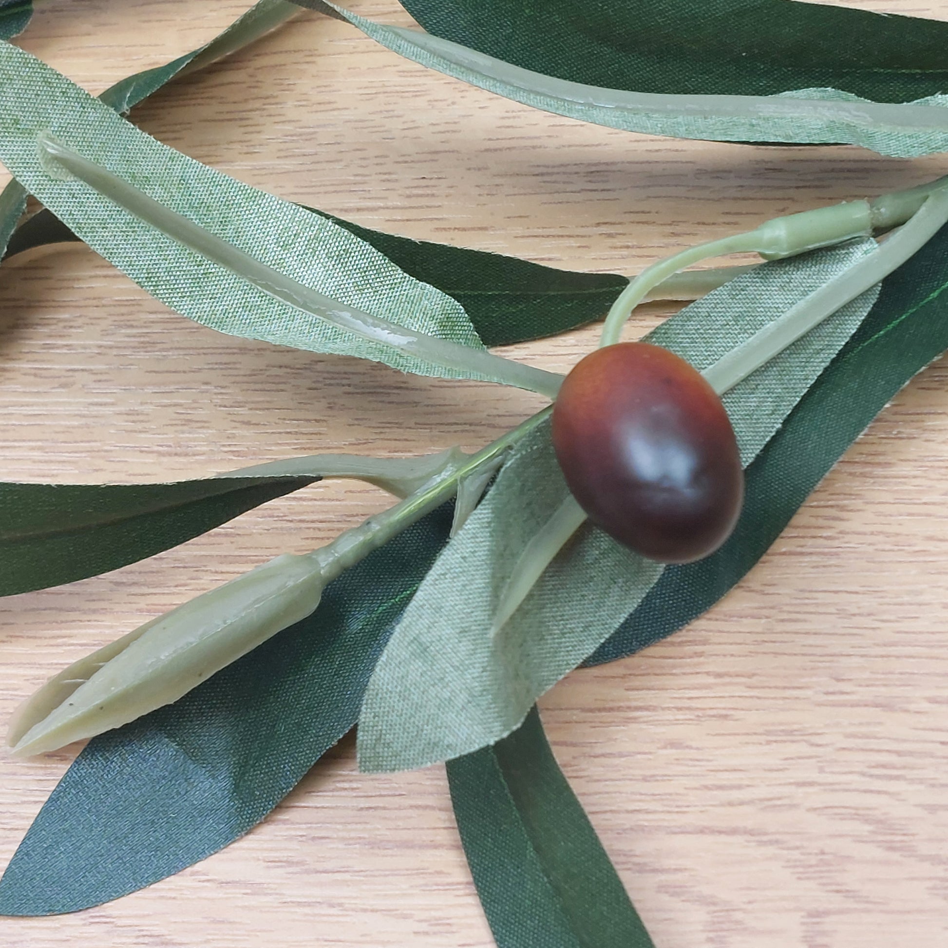 Close up of Artificial green olive leaves with a single brown olive fruit on a wooden surface
