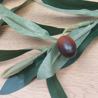 Close up of Artificial green olive leaves with a single brown olive fruit on a wooden surface