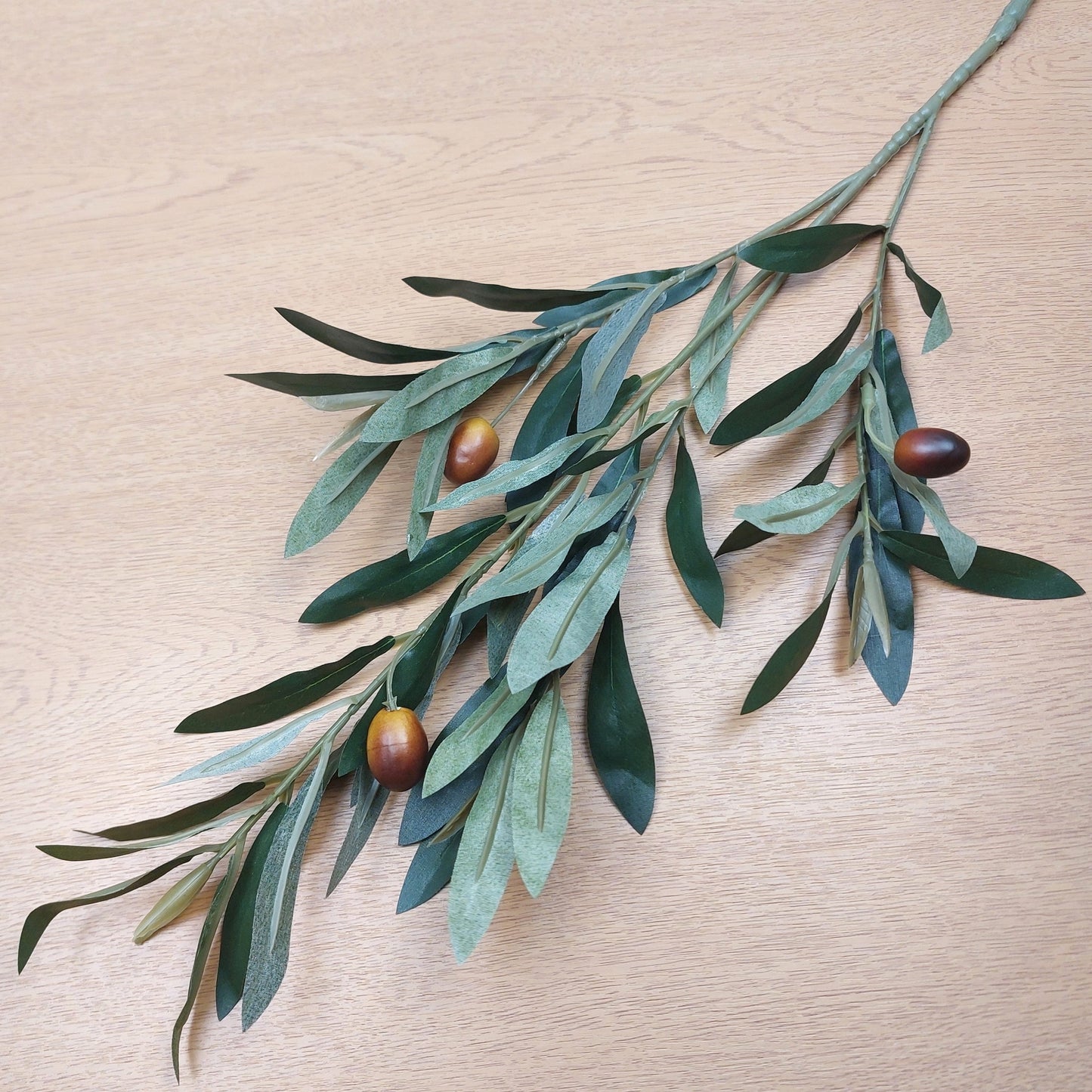 Artificial Olive branch with green leaves and brown olives on a wooden surface