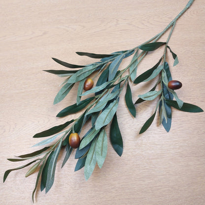 Artificial Olive branch with green leaves and brown olives on a wooden surface