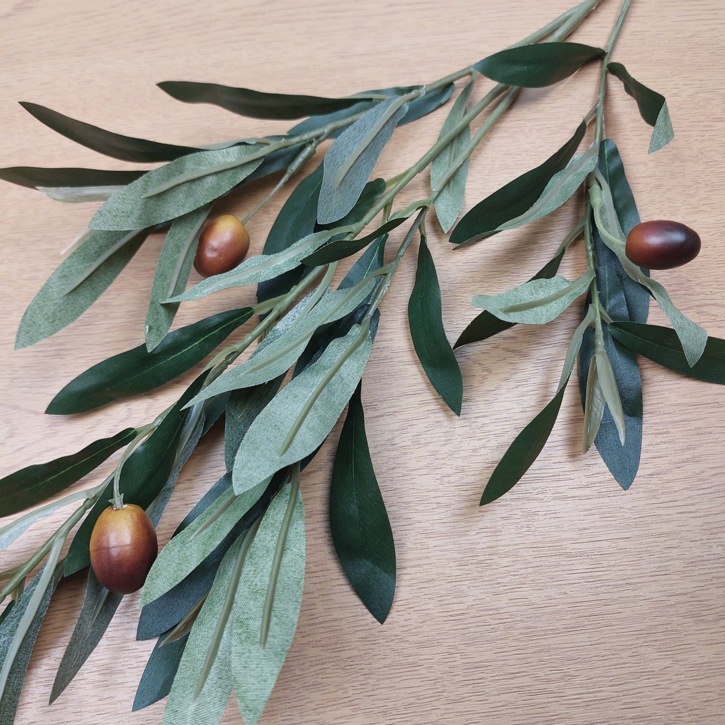 Artificial Olive branch with green leaves and brown olives on a wooden surface