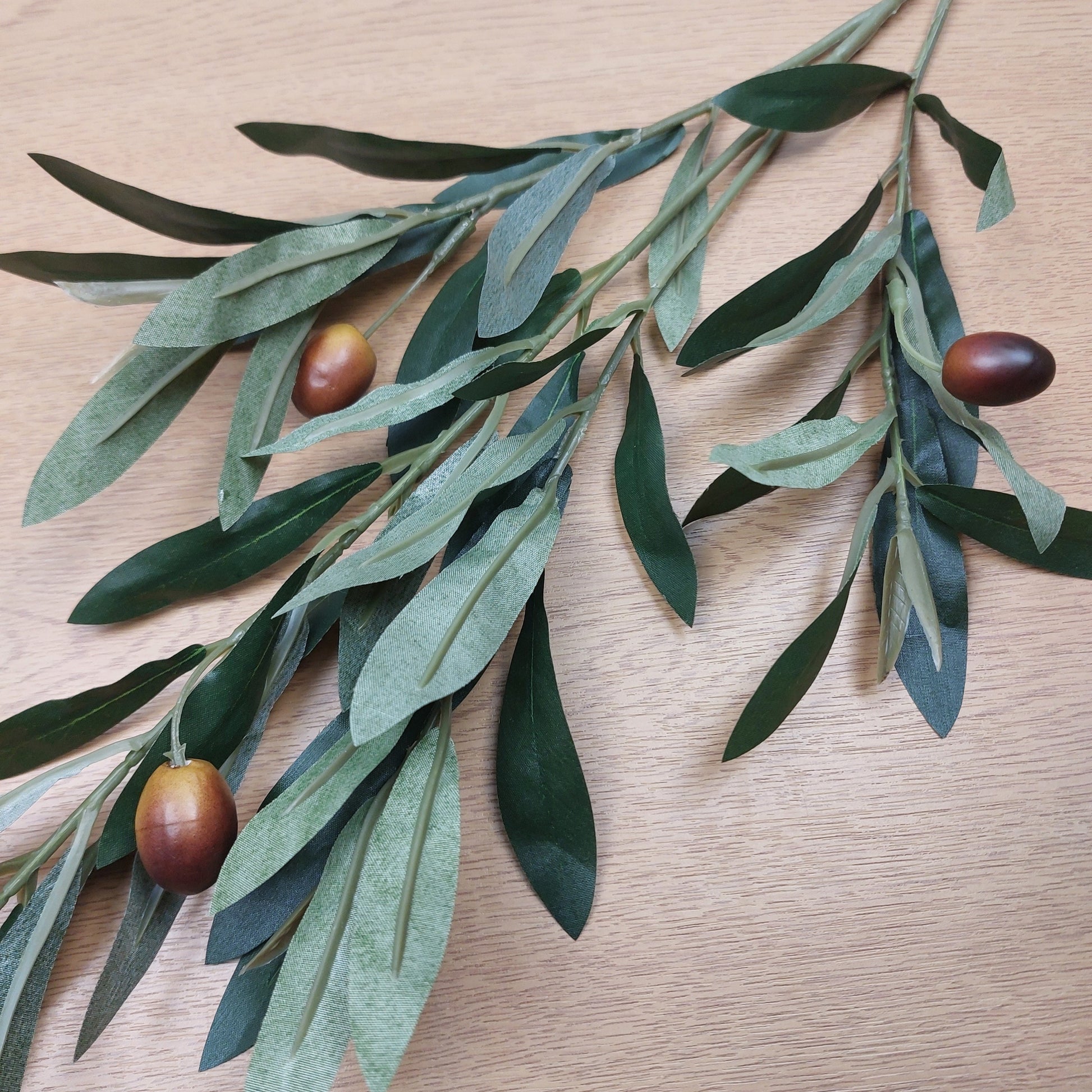 Artificial Olive branch with green leaves and brown olives on a wooden surface