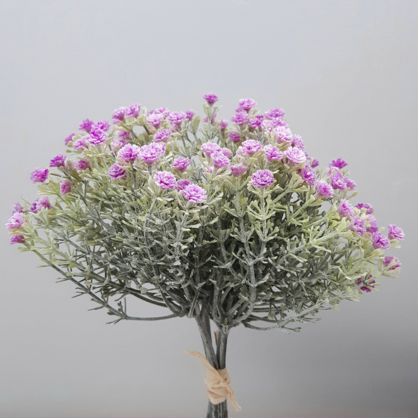 A bunch of artificial lilac open gypsophila flowers with green leaves and purple flowers, tied together at the bottom.