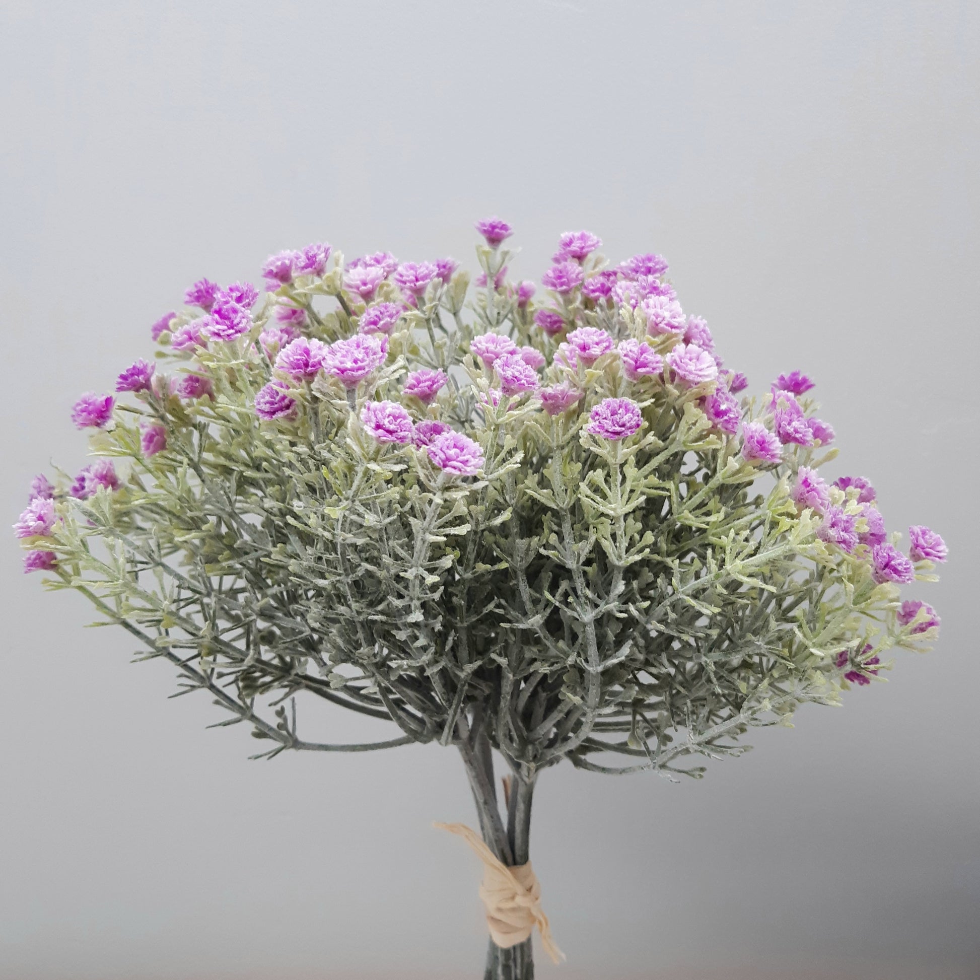 A bunch of artificial lilac open gypsophila flowers with green leaves and purple flowers, tied together at the bottom.