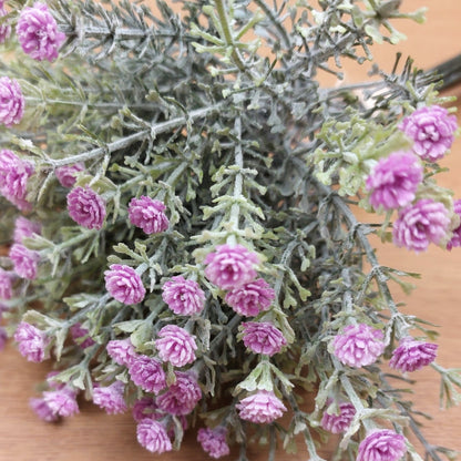 Close-up of artificial lilac and pink baby's breath flowers with green leaves on a wooden surface