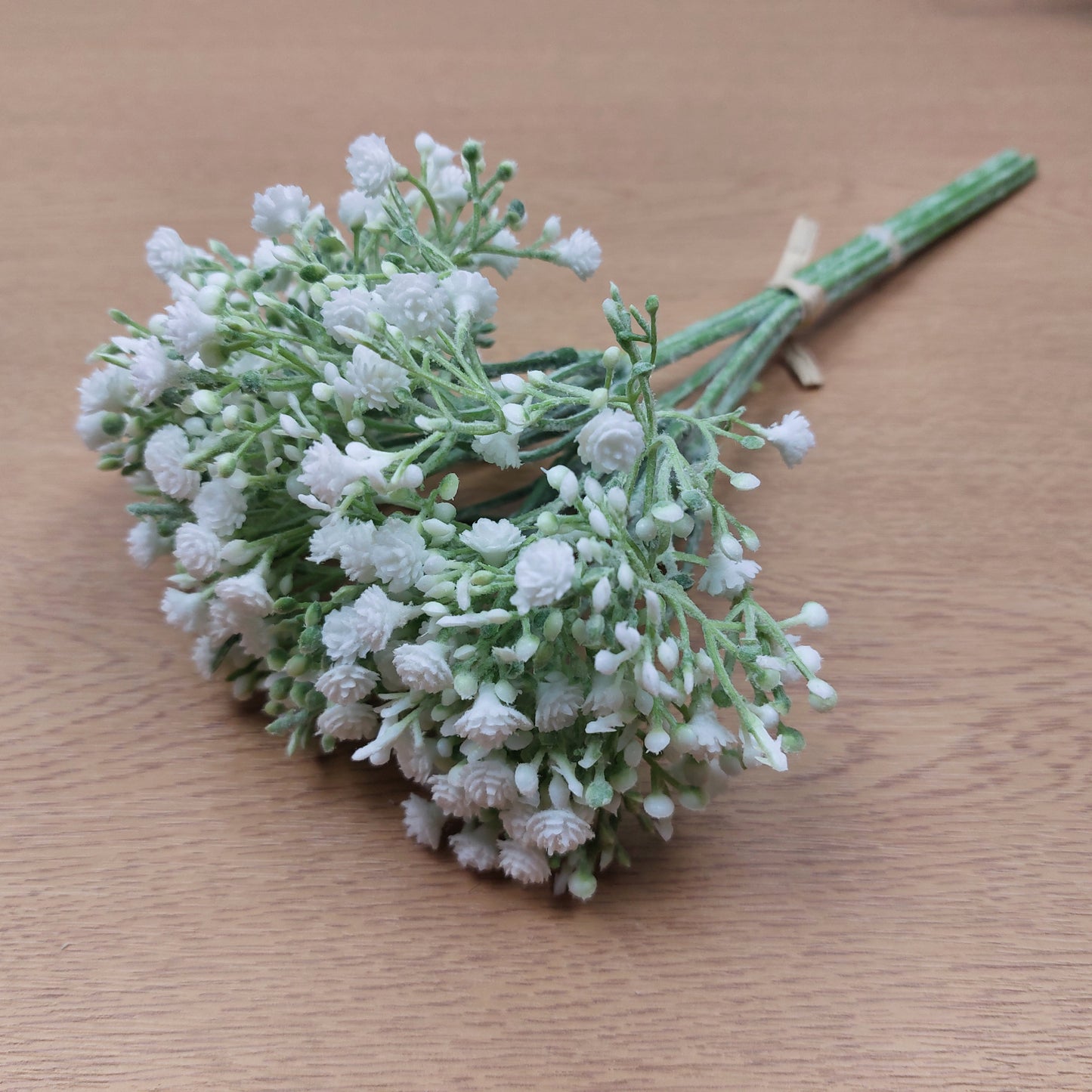A bunch of artificial White Gyp with open flowers and buds laying down on a wooden background