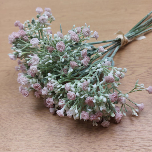 An Artificial Gyp bunch of pastel pink flowers with white buds against a wooden background