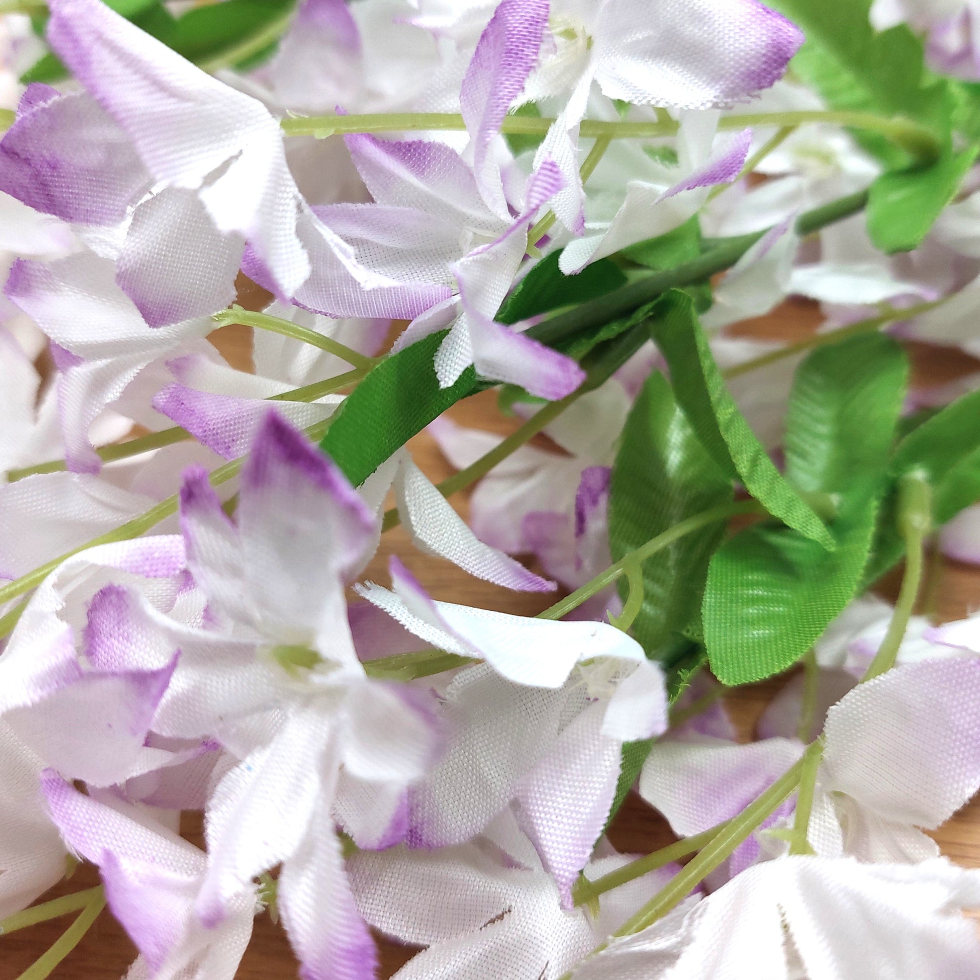 Close-up of white and purple periwinkle artificial flowers with green leaves on a wooden surface.