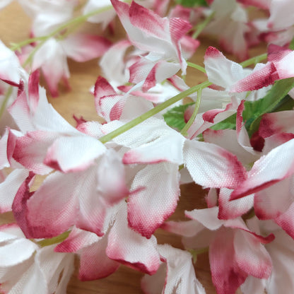 Close-up of artificial pink and white periwinkle flowers with green leaves on a wooden surface
