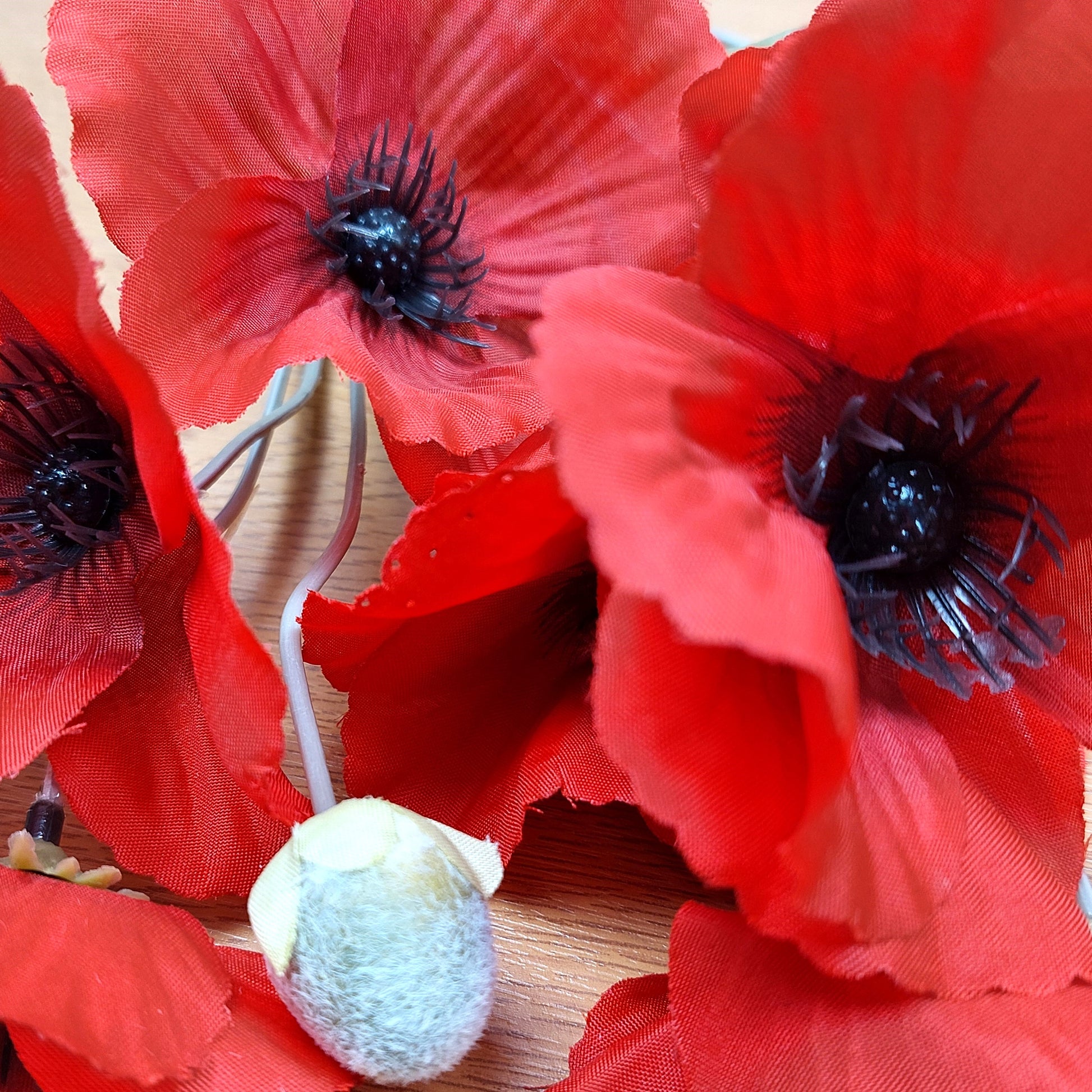 Close-up of artificial red poppies with a pale green bud on a wooden background.