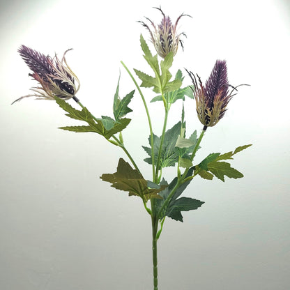 An artificial flower stem featuring three purple Eryngium thistle heads with green leaves on a plain light gray background.