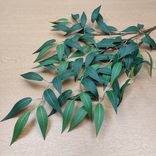 Green artificial ruscus leaves on a stem spray on a wooden surface