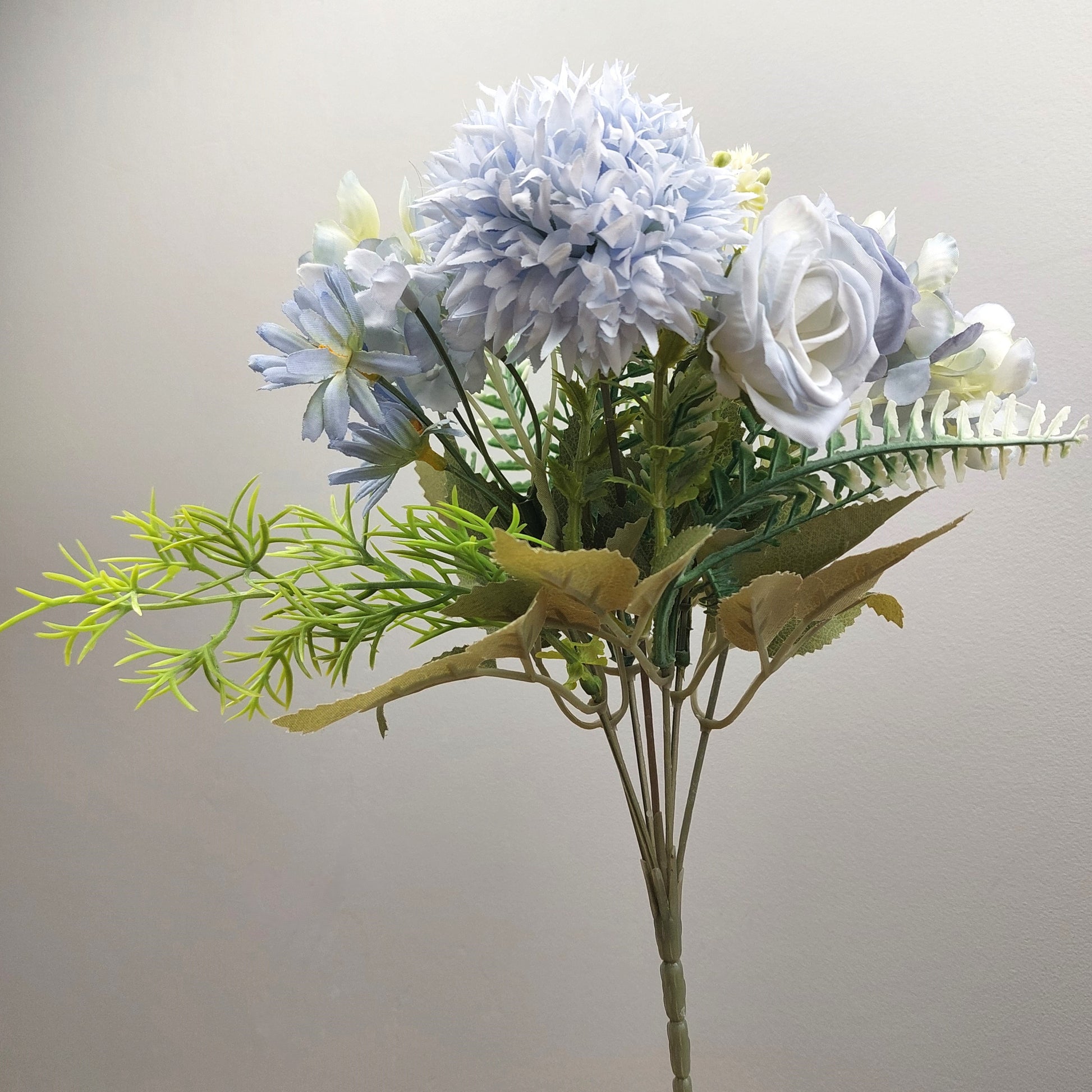 An artificial flower bouquet featuring light blue and white flowers with green and yellow foliage, set against a plain light gray background.