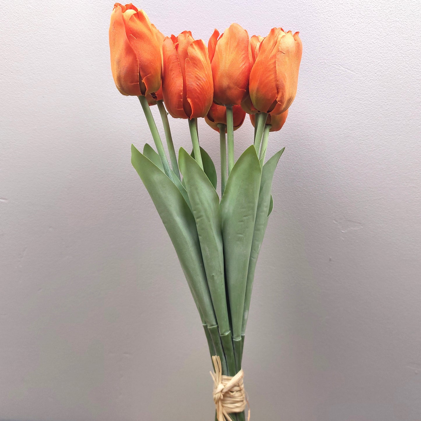 A bunch of artificial Orange Tulips against a pale background