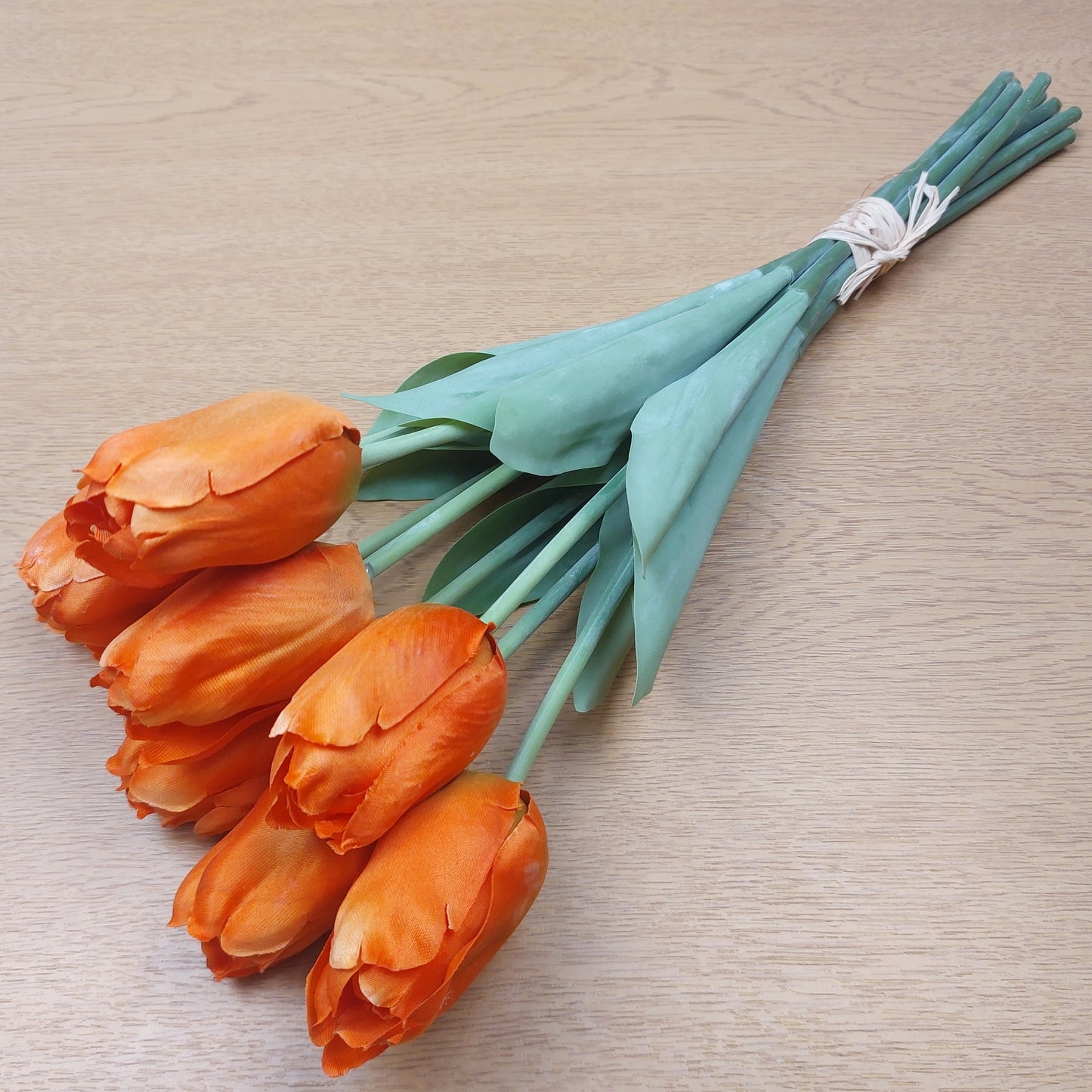 An Orange bunch of artificial Tulips against a wooden background 