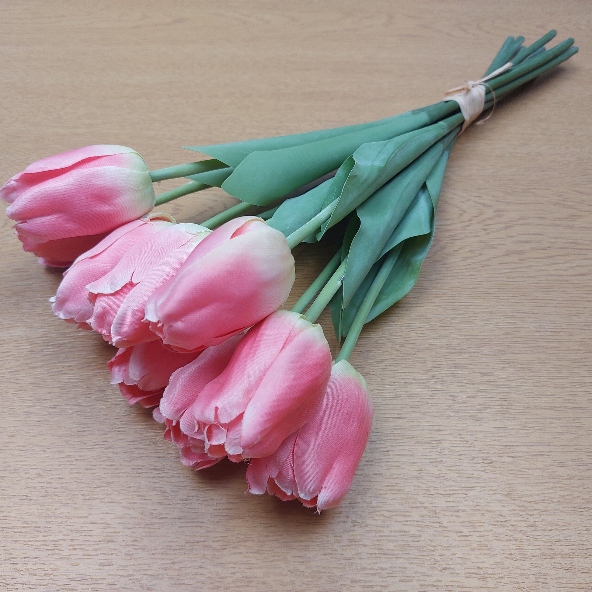 A bunch of artificial Pink Tulips laying down against a wooden background