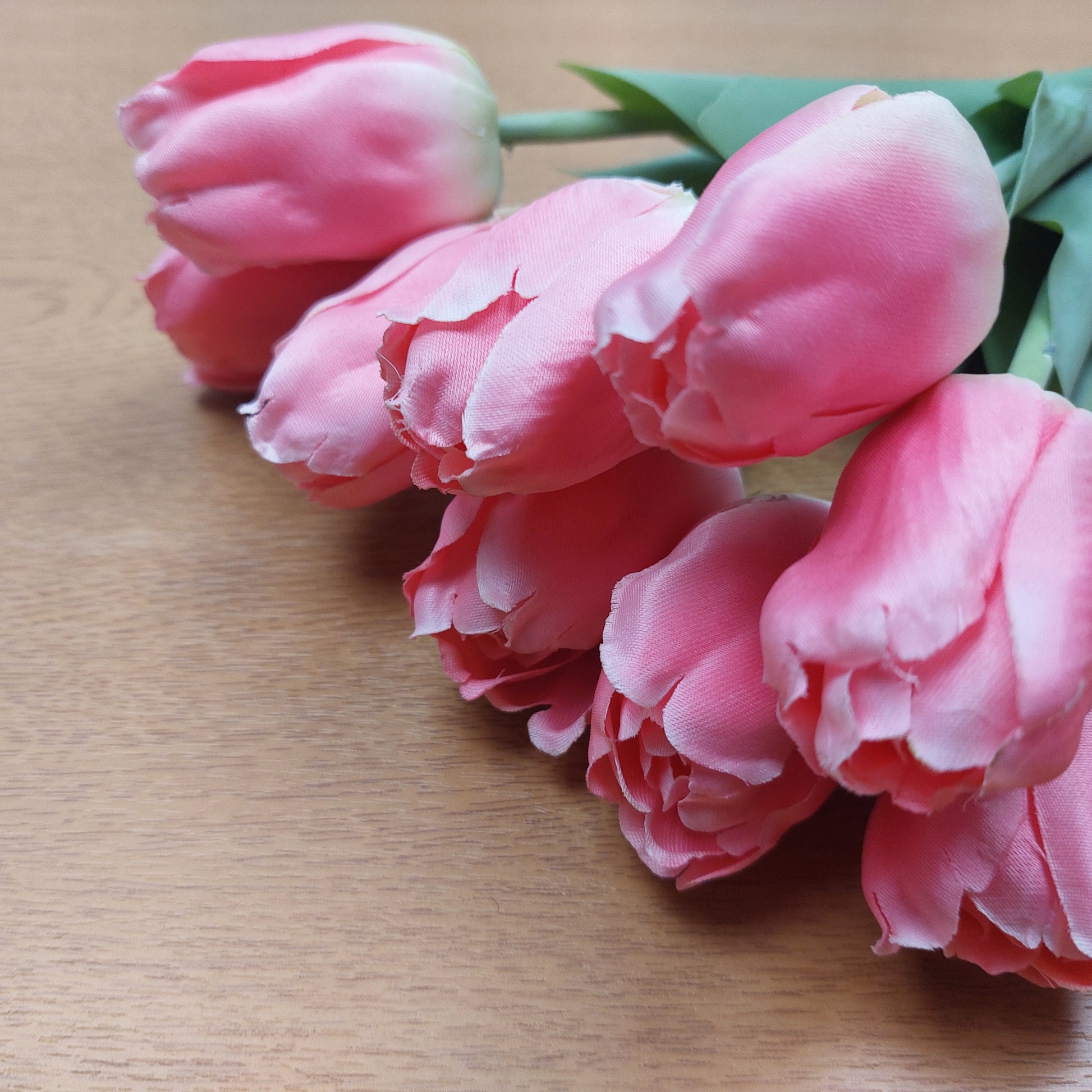 A close up of Pink Artificial Tulips laying down on a wooden background