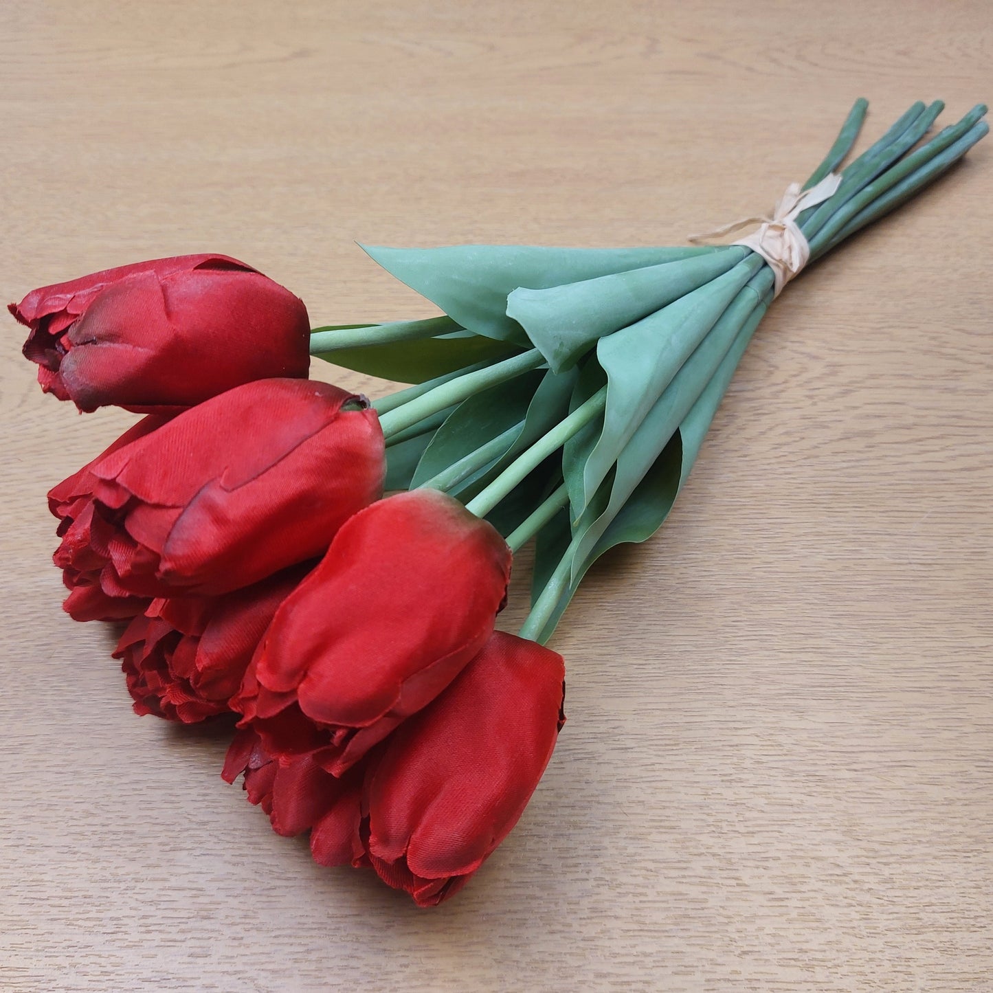 A bunch of Artificial Red Tulips laying down on a wooden background