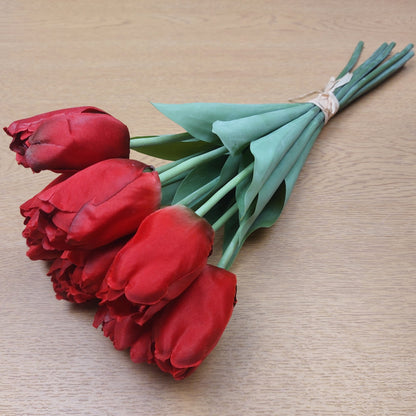 A bunch of Artificial Red Tulips laying down on a wooden background