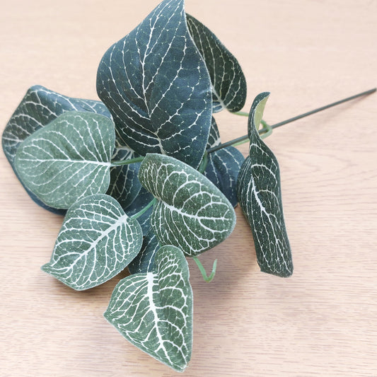 A stem of artificial green and ivory Fittonia leaves against a wooden background