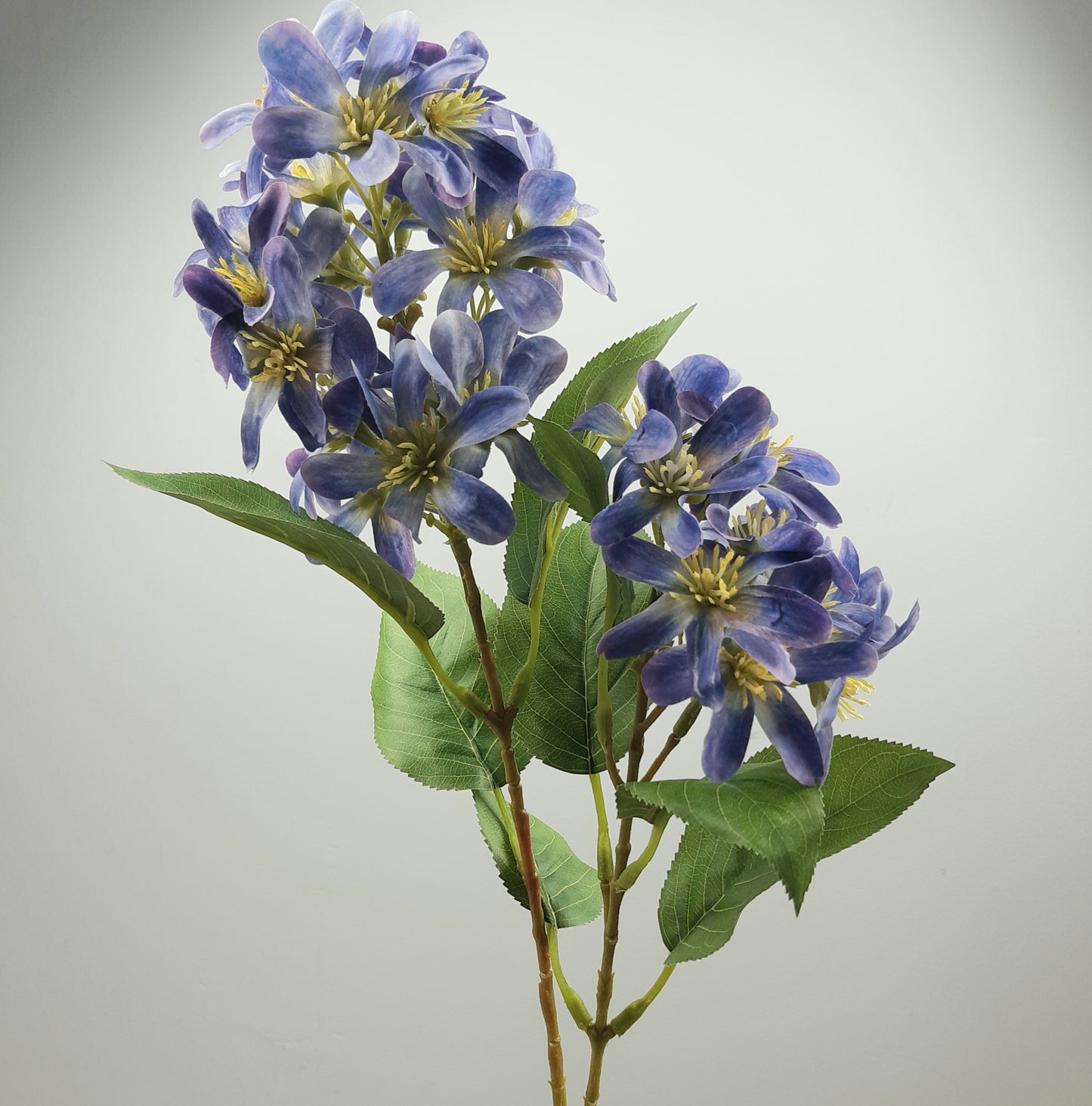 Artificial blue and purple faux vernicia flower spray with green leaves on a grey background