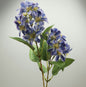 Artificial blue and purple faux vernicia flower spray with green leaves on a grey background