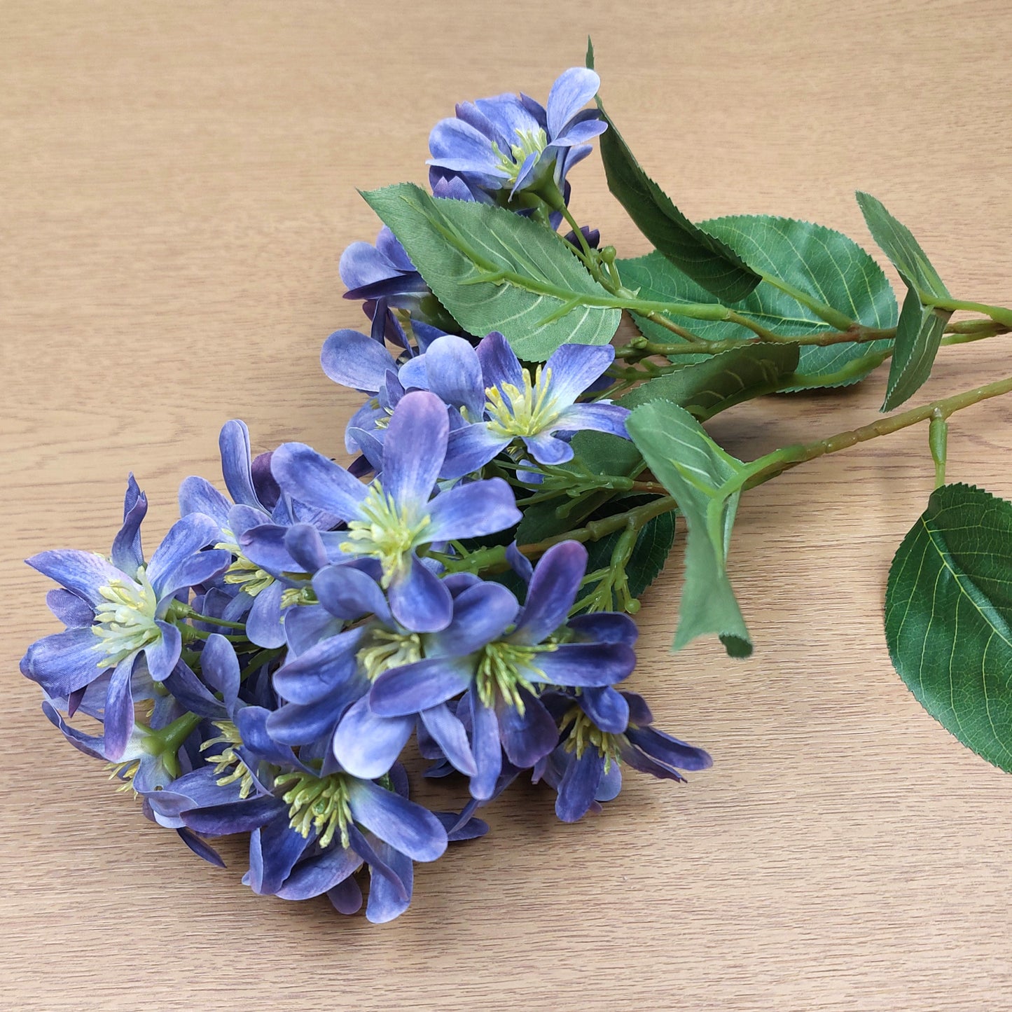 Bouquet of artificial blue and purple Vernicia Tung Blossom flowers with green leaves on a wooden surface