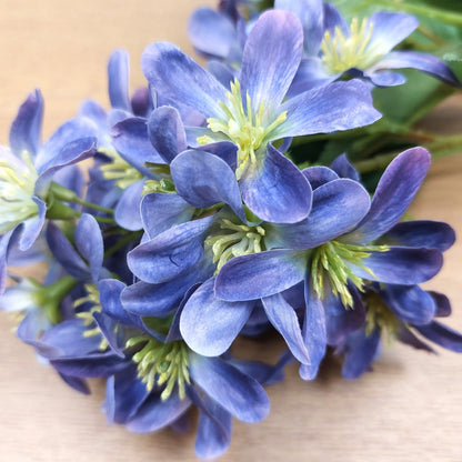 Close-up of artificial blue and purple flowers with green centers on a wooden surface